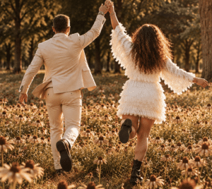 Stel loopt hand in hand door een veld met madeliefjes, van achteren gefotografeerd. Symbolisch beeld bij een blog over 25 jaar samen en waarom geen enkele relatie perfect is.